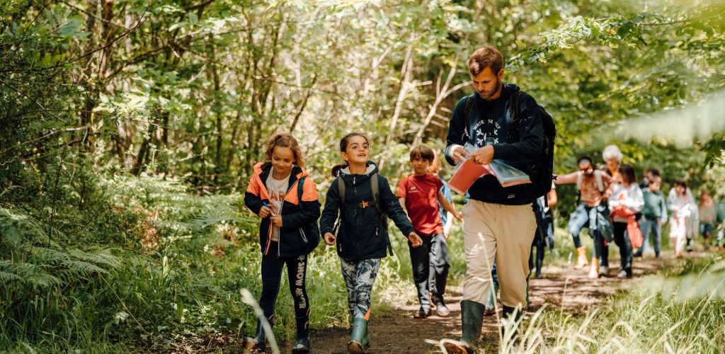 Virgile, animateur de l’antenne Vendée, est entouré d'une classe d'élèves dans la forêt, pendant une séance Water Forest School.